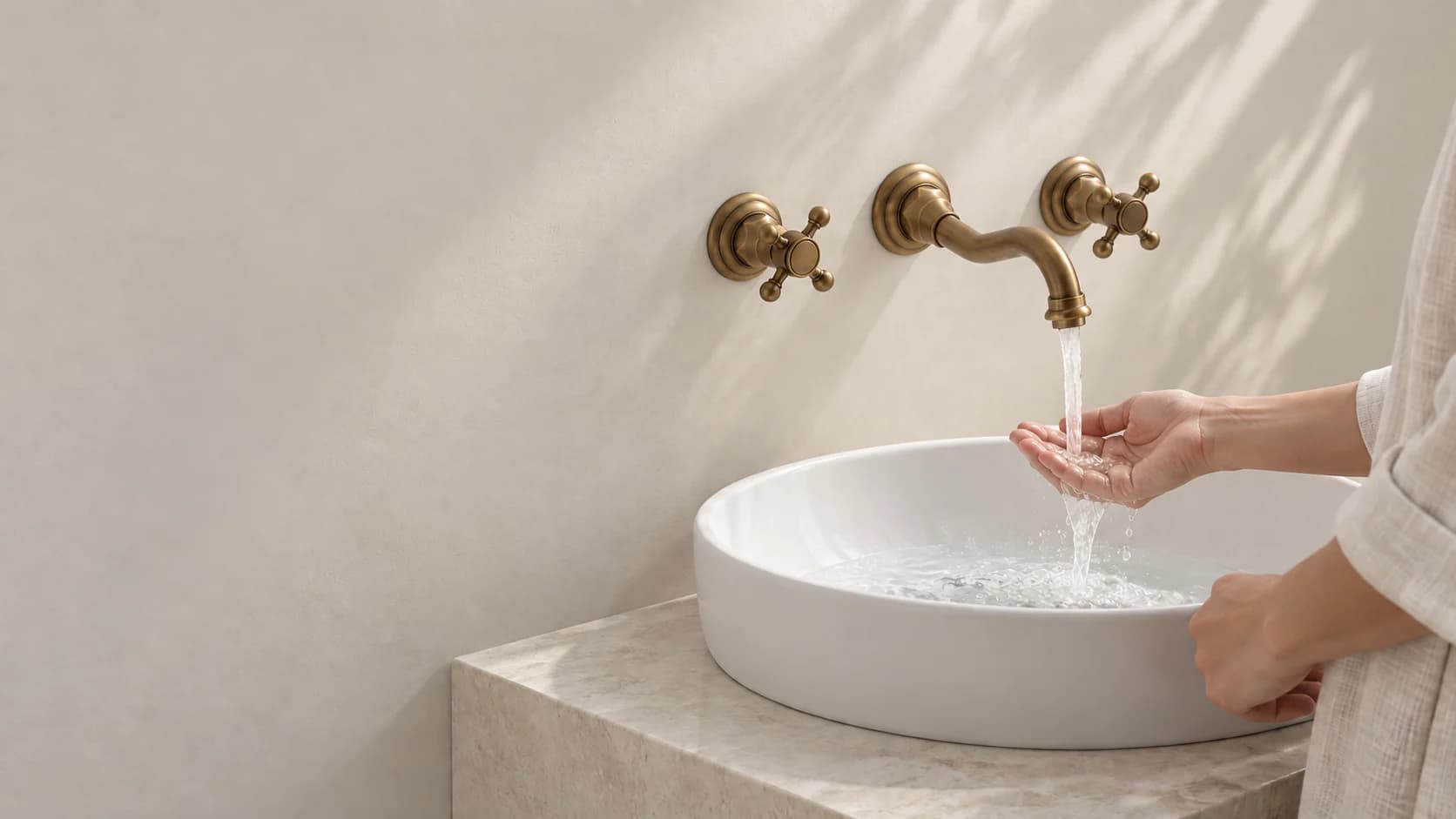 Wandmontierte Badarmatur EYN AQ0732 in Antikmessing über einem Waschbecken; rechts prüft eine erwachsene Person den Wasserstrahl.